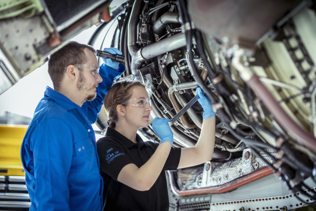 A female mechanic being supervised by a male mechanic working on an engine